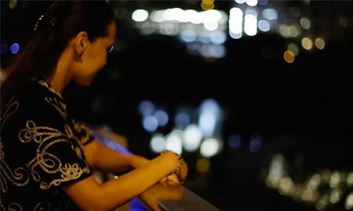 Kazakh woman in traditional clothing looks over a bridge at night